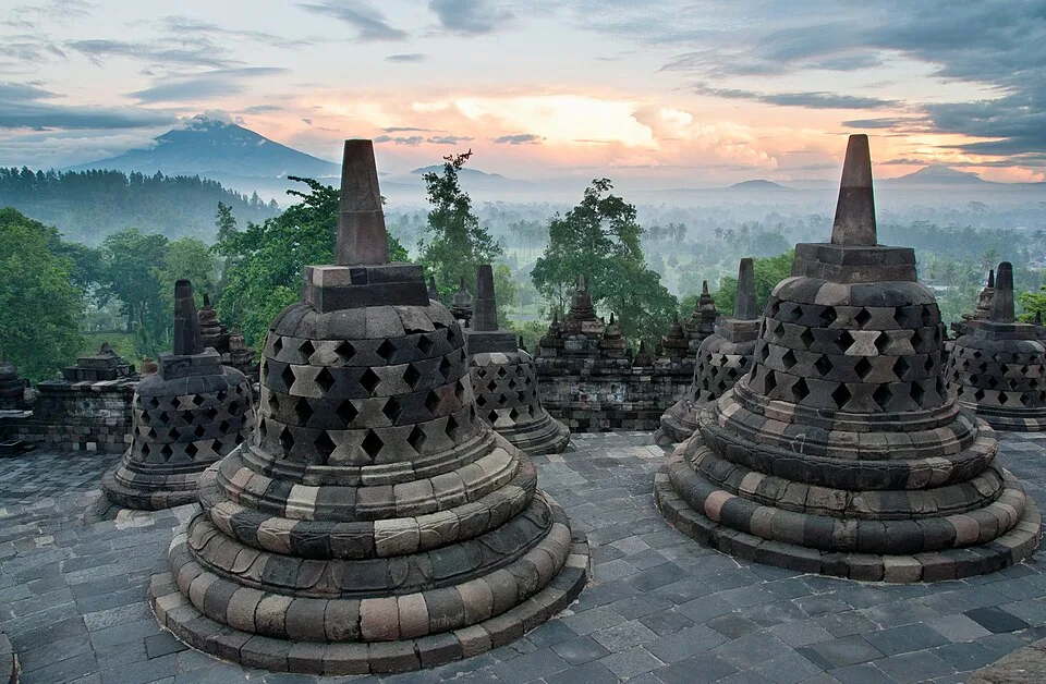 Stupas de pierre de Borobudur au premier plan, avec des montagnes dans la brume au loin.