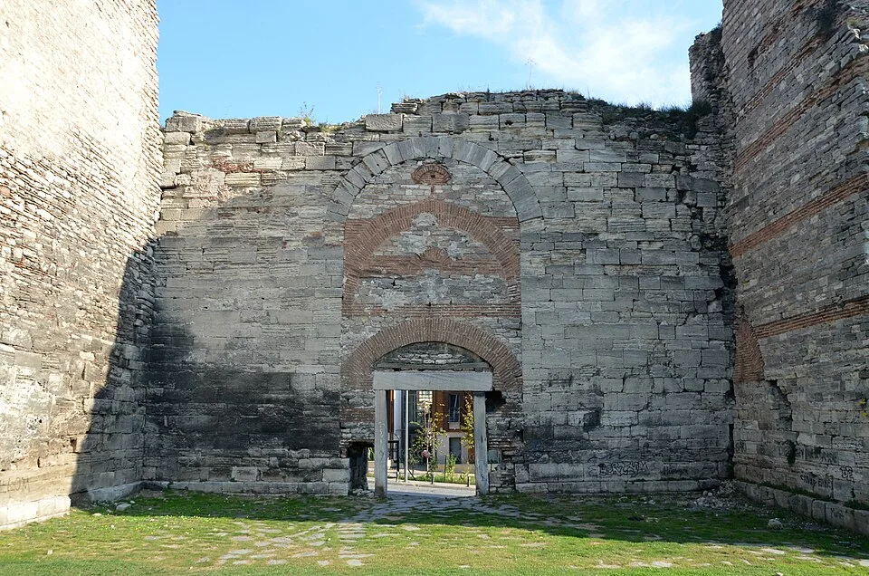 Une porte en arc de brique perce un épais mur de pierre, entre deux parties saillantes des murailles de Constantinople.
