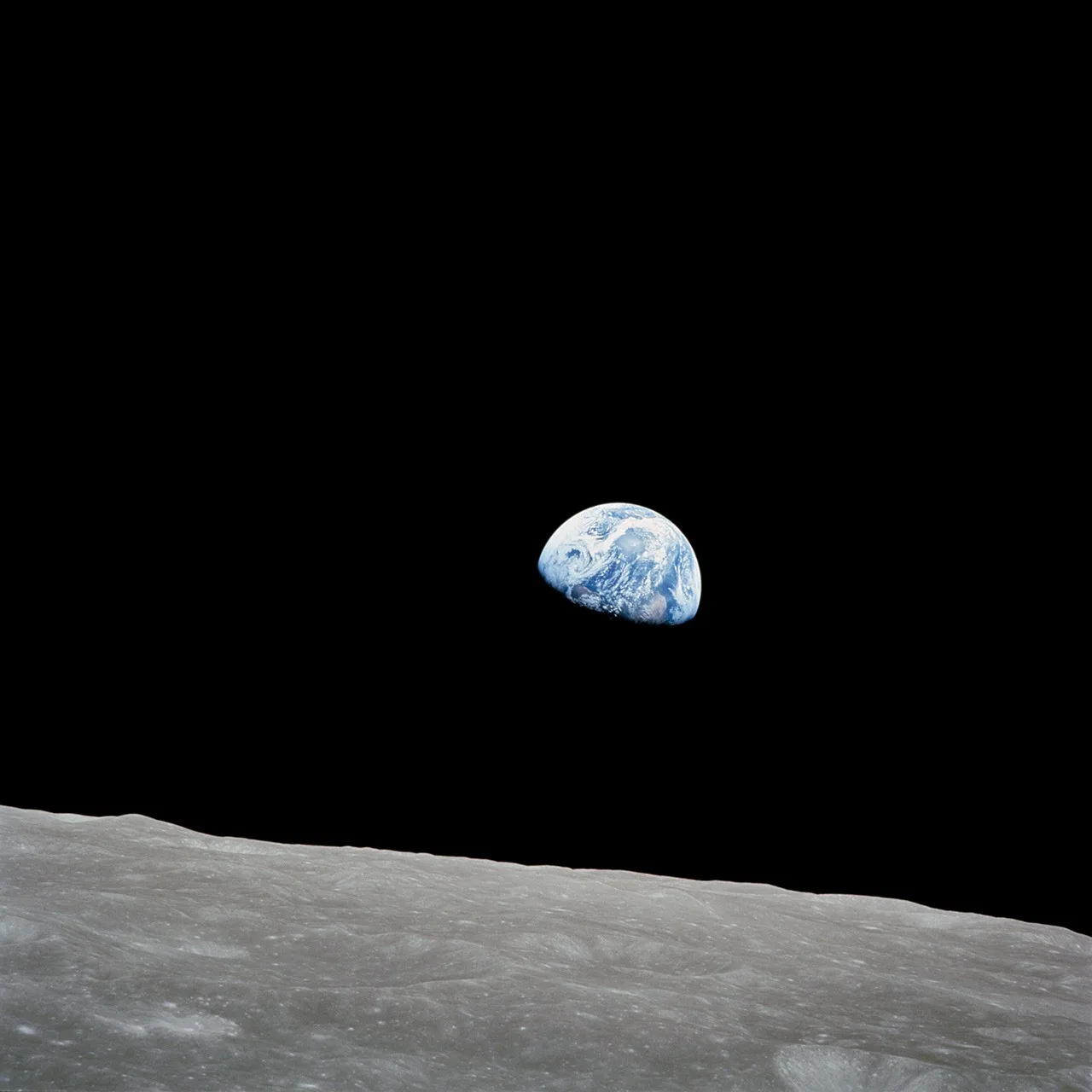 La Terre bleue et blanche se détache sur un ciel noir au-dessus d’un horizon lunaire gris.