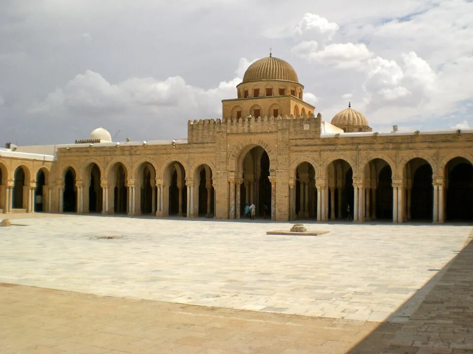 Une vaste cour pavée bordée d’arcades, avec un dôme au centre du portique de la Grande Mosquée de Kairouan.